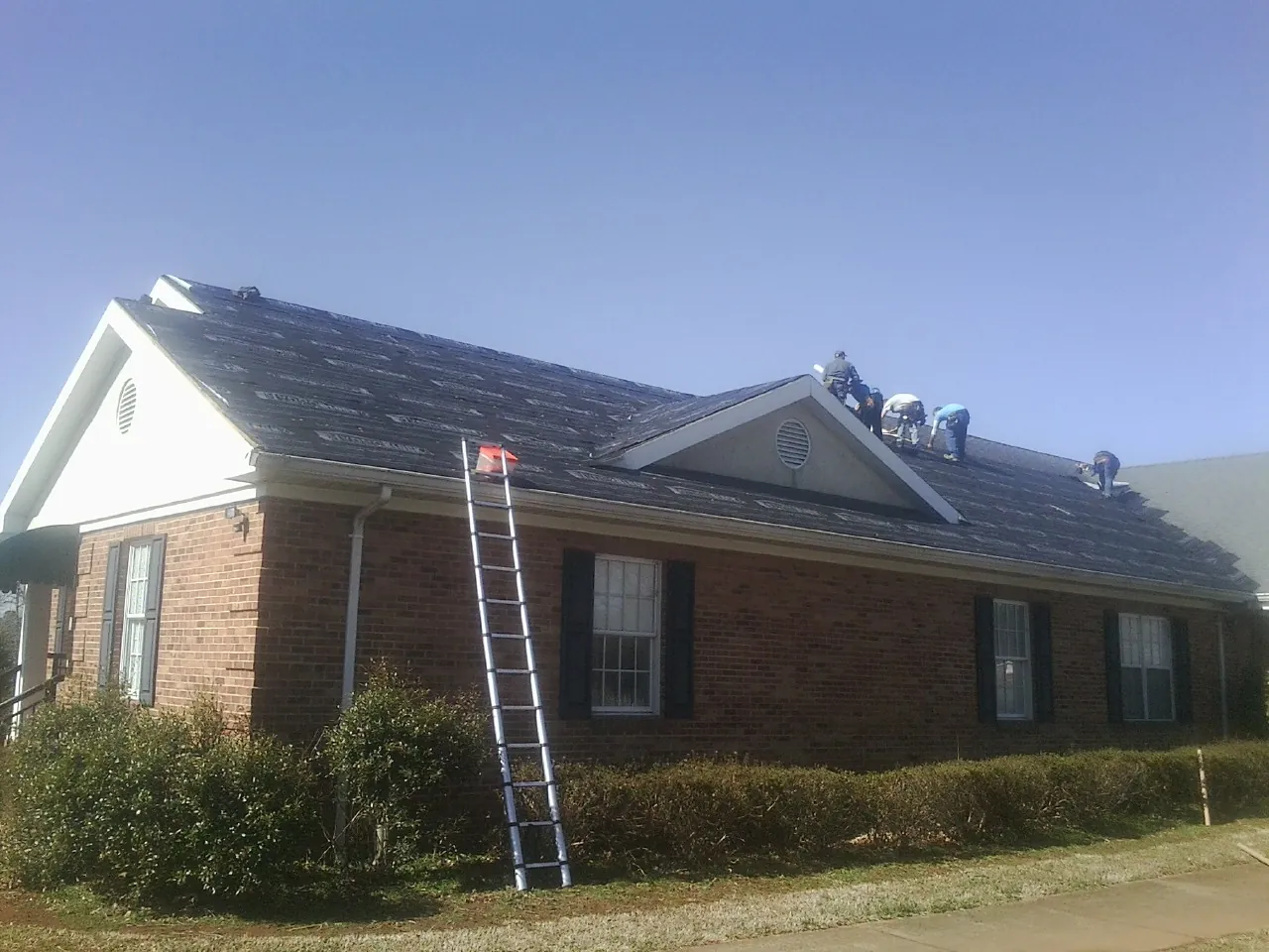 Crew tearing shingles off a brick ranch roof with a ladder set — Metal Roof Repair work by our crew in Helmetta