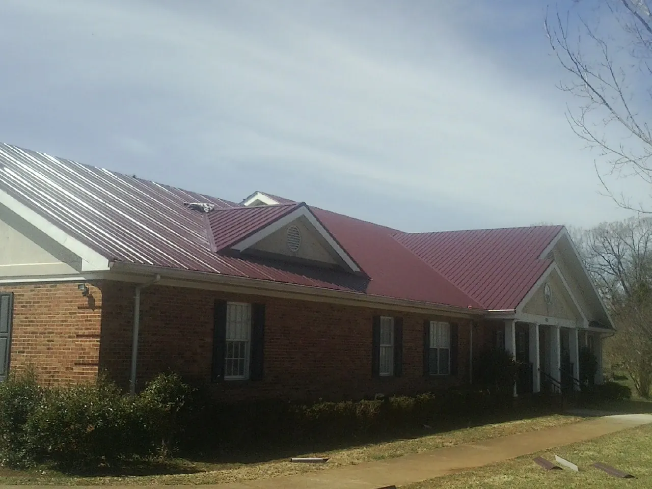 Red metal roof with gabled entries on a long brick building, from a Hail Damage Roof Repair job in Helmetta