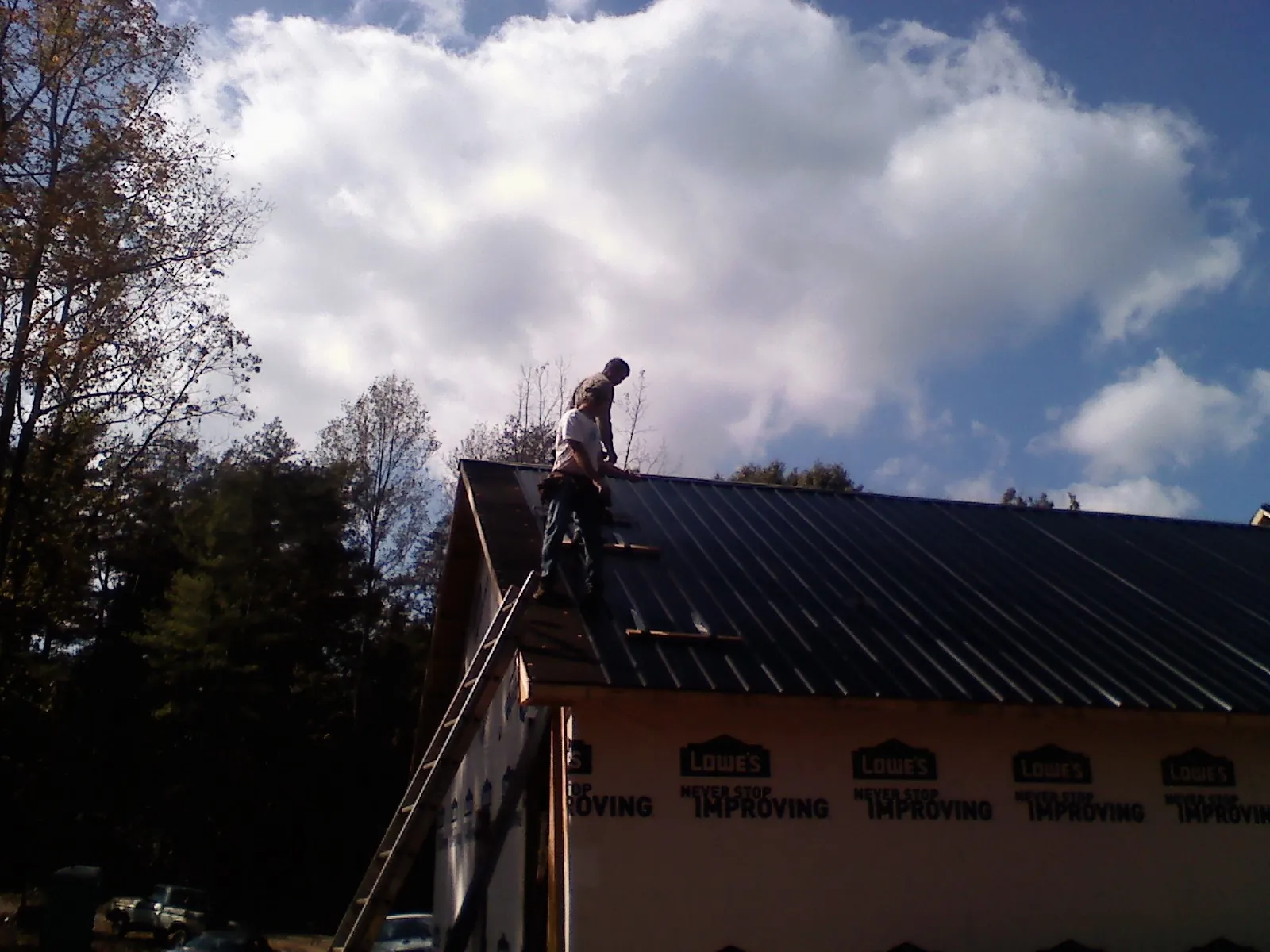 Roofer fastening dark metal panels high against a cloudy sky, from a Roof Inspection job in Helmetta