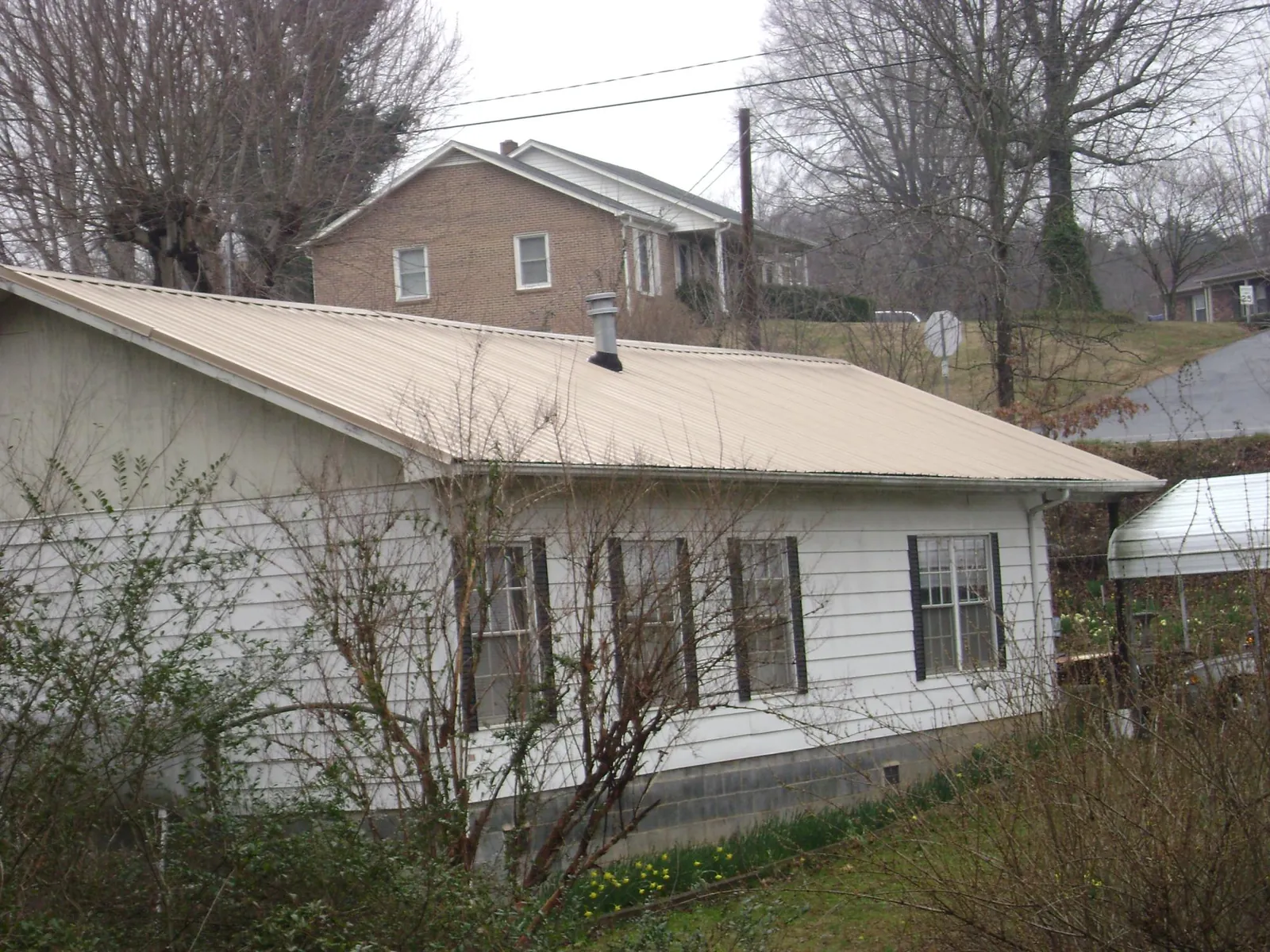 Tan metal roof on a white sided house set into a hillside — Commercial Roofing by Roofing Brothers in Helmetta